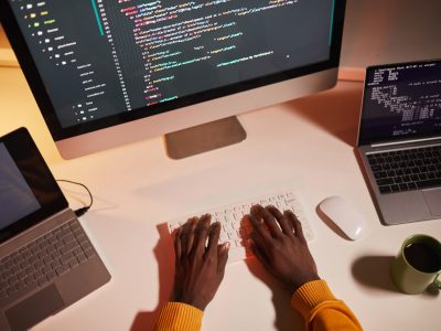 Top view close up of unrecognizable African-American man writing code while working with multiple computer screens, copy space