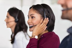 Multiethnic colleagues working in a call center. Team of business people sitting in a row working in a call center. Smiling customer support operator at work. Smiling young middle eastern woman with headset working at helpdesk.